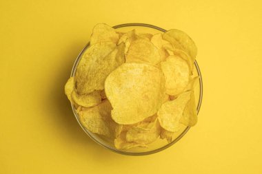 Sarı arka planda yuvarlak bir kasede patates cipsi. Üst Manzara. En popüler atıştırmalık. Abur cubur.