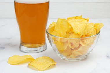 Patates cipsi ve bir bardak light birayla birlikte derin bir cam kasenin yakın çekimi. Popüler bira atıştırmalığı.