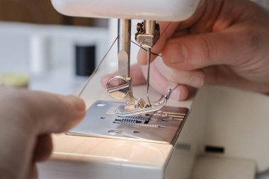 Terzi elektrikli dikiş makinesinin ipliğini kesiyor. Elleri yakın çekim. Terzi iş akışı detayları.