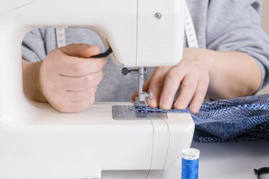 Terzi, elektrikli dikiş makinesine dikiş atıyor. Elleri yakın çekim. Terzi iş akışı detayları.