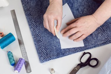 Terzi, kağıt desenine göre tebeşirle bir kumaş parçasına işaret koyuyor. Yukarıdan bak. Bir terzinin işi, dikiş ve kıyafet yapmak için aletler..