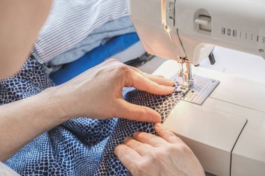 Terzi, elektrikli dikiş makinesine dikiş atıyor. Elleri yakın çekim. Terzi iş akışı detayları.