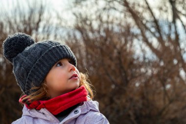 Little girl in a woolen hat and red scarf playing in the field. Little girl with winter clothes