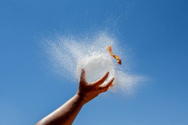 Water filled balloon explodes on a hand with the blue sky in the background. Childish games. refreshing games. Explosion of a balloon.