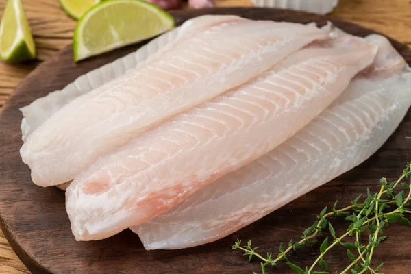Çiğ tilapia balığı fileto ve ahşap masa üzerinde baharatlar.