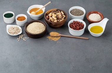 Taş zemin üzerinde fotokopi alanı olan kaşıklarla çeşitli süper yiyecekler. Chia, kinoa, yulaf, keten tohumu, bal, spirulina ve diğerleri..