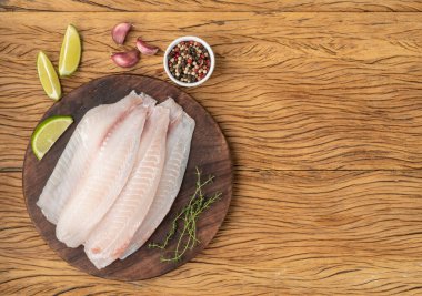 Çiğ tilapia balığı filetosu, ahşap masa üzerinde baharatlar ve fotokopi alanı..