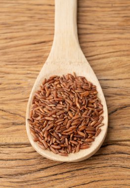 Ahşap bir masanın üzerinde bütün pirinci kaşık içinde ham kırmızı renkte..