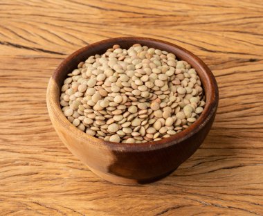 Tahta masanın üzerinde bir kasede çiğ mercimek.