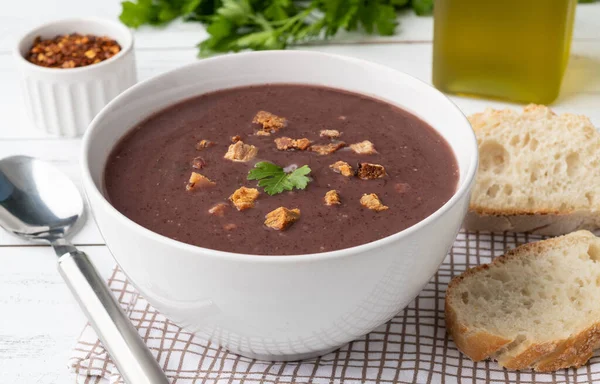Siyah fasulye çorbası, ekmek dilimleri ve ahşap masa üzerinde baharat..