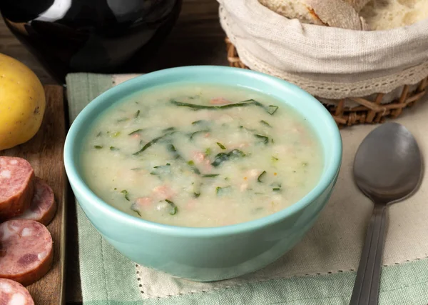 Traditional portuguese green soup with potato, green cabbage and sausage in a bowl with bread and wine.