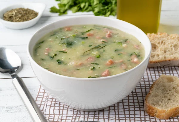 Traditional portuguese green soup with potato, green cabbage and sausage in a bowl with bread.