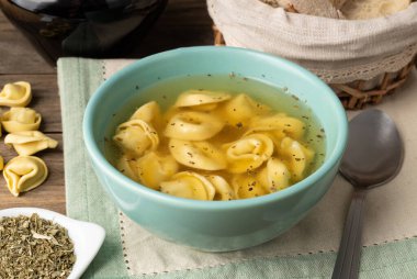 Cappelletti ya da tortellini brodo çorbası ekmek dilimleri ve ahşap masa üzerine baharat katılmış..
