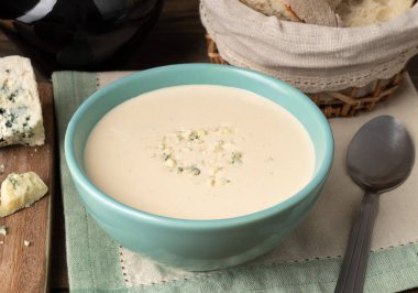Tabakta peynir çorbası, ekmek dilimleri ve ahşap masada şarap..