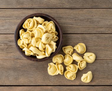 Ahşap bir masanın üzerinde pişmemiş kapel ya da tortellini..