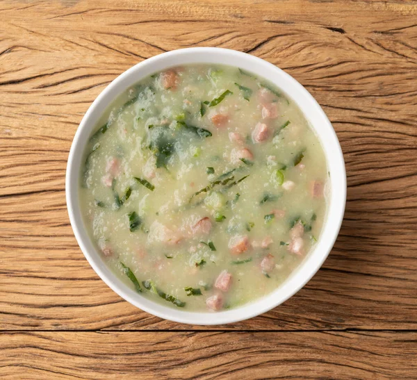 Traditional portuguese green soup with potato, green cabbage and sausage in a bowl over wooden table.