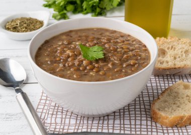 Kahverengi mercimek çorbası, ekmek dilimleri ve ahşap masa üzerinde baharat..