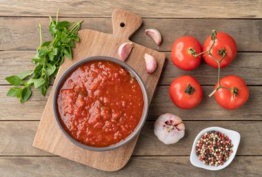 Domates sosu, domates, sarımsak, zeytinyağı ve otlar ahşap masanın üzerinde..