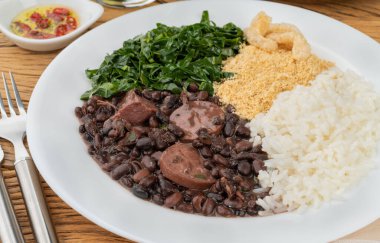 Typical brazilian feijoada with rice, pepper, farofa, kale and cracklings.