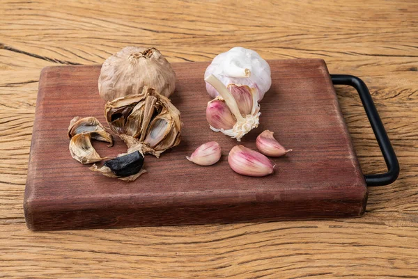 Fermented black garlic and regular garlic bulbs and cloves over wooden table.