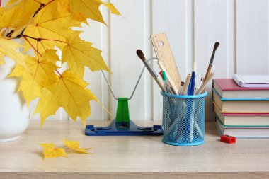 Okul sonbaharı kırtasiye malzemeleri ve sarı akçaağaç yapraklarıyla dolu.