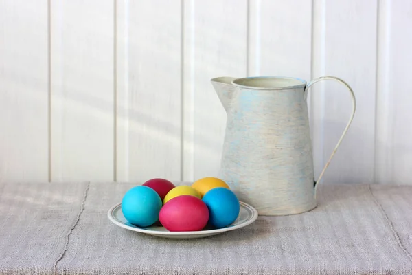 Ηλιόλουστη Πασχαλινή ζωή με πολύχρωμα αυγά και μια κανάτα. — Φωτογραφία Αρχείου
