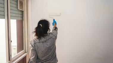 Genç Latin kadın dairesinde duvar boyuyor.