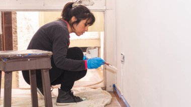 Küçük bir fırçayla resim yapan genç Latin kadın dairesinde bir duvar var.