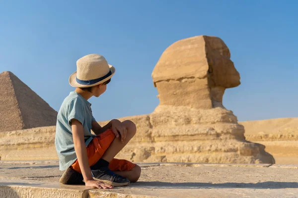 The boy in hat sits in front of the sphinx and looks at it — Stock Photo, Image
