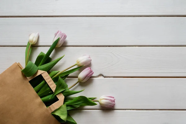 Bouquet primavera di tulipani rosa in sacchetto di carta beige su sfondo di legno — Foto Stock