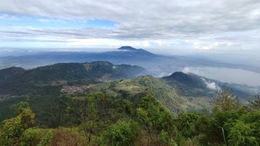 Güzel dağ manzarası ve mavi gökyüzü. Güneşli bir günde dağlara. Sabah ışığında dağ çayırında. Çimenli tepenin arkasındaki ormanın arkasında sisli bir vadi ile ilkbahar manzarası. Parlak mavi gökyüzünde kabarık bulutlar. Doğa tazeliği