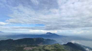 Güzel dağ manzarası ve mavi gökyüzü. Güneşli bir günde dağlara. Sabah ışığında dağ çayırında. Çimenli tepenin arkasındaki ormanın arkasında sisli bir vadi ile ilkbahar manzarası. Parlak mavi gökyüzünde kabarık bulutlar. Doğa tazeliği