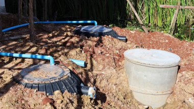 Black PE septic tank. Plastic septic tank and cement pipe are buried in the soil and PVC pipe is connected to treat waste in outdoor construction site with copy space. selective focus clipart