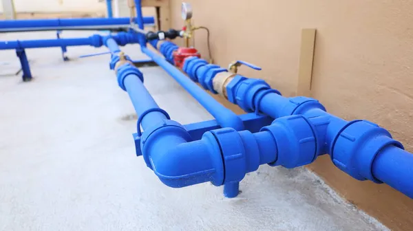 Tesisat ve tesisat sistemleri. Çimento arka planında yüksek binaların duvarlarının yanında valfleri olan mavi su boruları. seçici odak