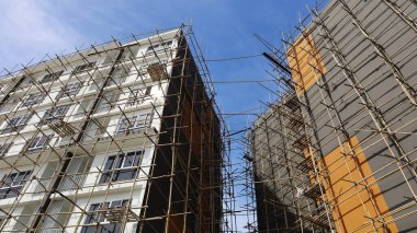 Çift katlı binanın yanında ahşap iskele. Bambu iskelesi binanın etrafına yenilenmeyi desteklemek ya da mavi gökyüzü arka planına karşı aşağıdaki manzarayı yeniden boyamayı desteklemek için kurulmuştur. Seçici odak