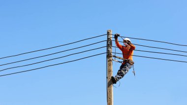 Elektrik direklerinin kablolarını bağlayan teknisyen. Çalışanlar elektrik direklerine, mavi gökyüzü arka planında fotokopi alanı olan beton direklere düşük voltajlı kablolar takmak için kemerleriyle asılılar. seçici odak