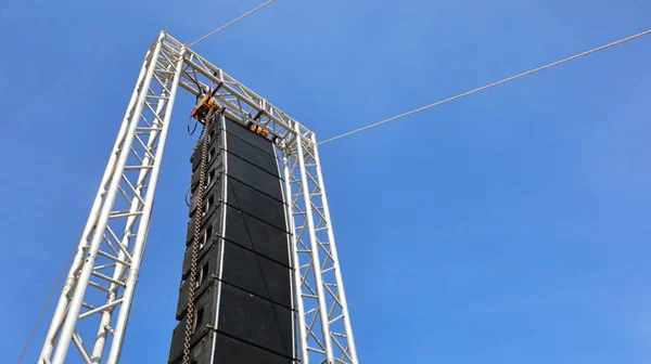 Kürsüde siyah bir hoparlör asılı. Alttaki beyaz metal bir çerçeveye asılı bir hoparlör seti parlak mavi bir gökyüzü arka planına karşı. seçici odak