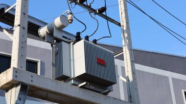 Beton kolon kirişlerinde trafo var. Yeşil ağaç zemininde yüksek voltajlı transformatör ve kopyalama alanı olan mavi gökyüzü. Yaklaş ve konuya odaklan.