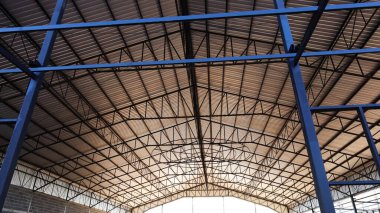 Çelik kolonlar ve çatı yapıları. Aşağıdaki manzarada metal levhalarla kaplı bir sanayi binasının çatısı. seçici odak