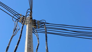 Beton direklerdeki elektrik kabloları. Beton kutupta düşük voltajlı iletim hattı açık mavi gökyüzü arkaplanında alt görünümde ve kopyalama alanı ile. seçici odak