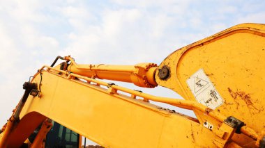 Hortumlu ve hidrolik silindirli kazıcı kolu. Beyaz bulutlu arka planda eski sarı kepçeli hidrolik sistem. Seçici odak