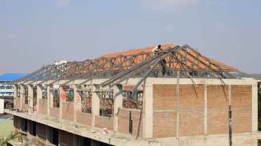 İnşaat halindeki binaların metal çatı yapısı. Bir erkek işçi mavi gökyüzü arka planında yeni bir bina için çelik bir yapı kuruyor. Seçici odak