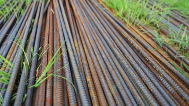 Yerde paslı bir demir yığını var. Deforme olmuş parmaklıkların yatay arkaplanı ve inşaat sahasında kısmen yeşil çimlerle kaplı bir inşaat demiri. Seçici odak