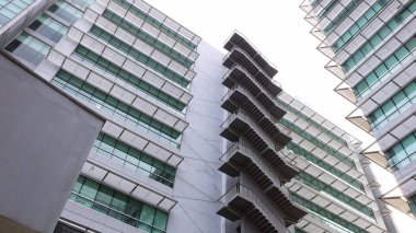 Binada yangın çıkışı var. Bir yangın merdiveni, alttaki yüksek bir binanın yanında asılı duruyor. Fotokopi alanı olan beyaz bir gökyüzü arka planında. Seçici odak