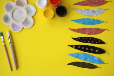 Kuru sonbahar yapraklarına elle boyanmış boya. Çocuk sanat projesi. Sarı arka planda boyanmış yapraklar. ÇEVİR
