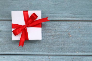 Mavi ahşap arka planda kırmızı kurdeleli beyaz hediye kutusu. Kutlama için. Sevgililer Günü gebeliği. Üst görünüm