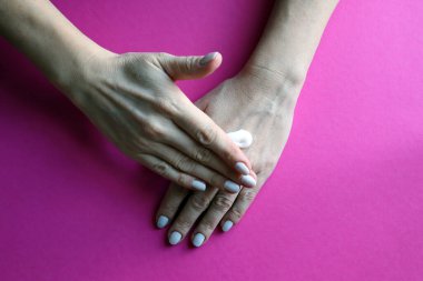 Ellerin derisinin soğuk mevsim koruması. Kadınların elleri koruyucu krem sürüyor. Pembe arka plan. Üst görünüm