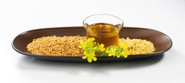 Beyaz arka planda hardal tohumu, yağ, püre ve çiçek. Yemek pişirmede ve vücut bakımında kullanışlı. Hardal tohumu ve çiçekli hardal bitkisi. Sorisha veya bilimsel adı Brassica.