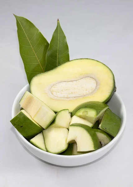 a bowl of raw green mangoes with mango leaves isolated on white background.