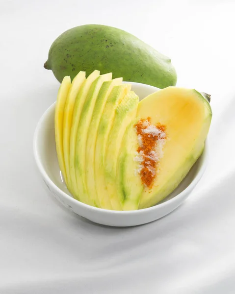 a unpeeled mango and mango slices with salt and chili powder. sour and sweet refreshing fruit in summer time.